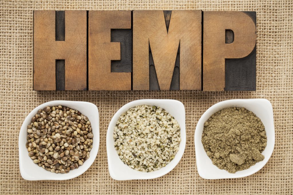 hemp products: seeds, hearts (shelled seeds) and protein powder in small ceramic bowls on burlap canvas with word hemp spelled in letterpress wood type